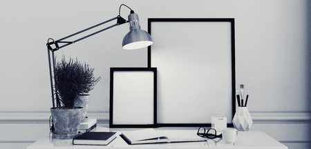 Blank picture frames on a simple modern desk or writing table with an open journal and anglepoise lamp in monochromatic black and white decor, 3d renderingの写真素材