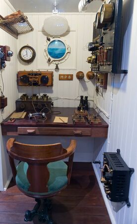 Museum exhibit display of communications room with tiny porthole, chair and various radios in old shipのeditorial素材