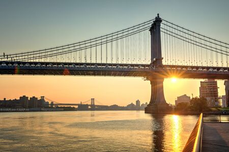 Gorgeous fiery orange sunset with a sunburst behind Brooklyn Bridge, New York, viewed across the water of the East River from a pierの写真素材