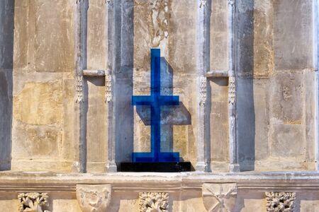 Colorful blue cross against an old stone wall with ornate carvings inside a church or cathedralの写真素材