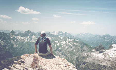 Man Sitting on Rock Ledge Enjoying the View and Serenity of Allgau Alps Mountain Ranges on Sunny Day with Blue Skyの写真素材