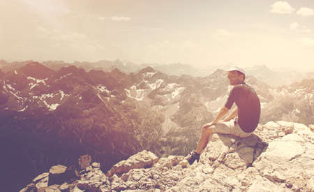 Male hiker sitting on a mountain summit during sunset enjoying the last sunrays and the beautiful mountain scenery. Image taken on the Hochvogel Mountain in Bavaria, Germany.の写真素材