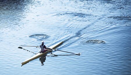 High angle view of a person sculling in a racing canoe on calm water moving diagonally through the...