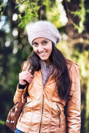 Waist Up Portrait of Attractive Young Indian Girl Wearing Leather Jacket and Wool Cap Smiling and...