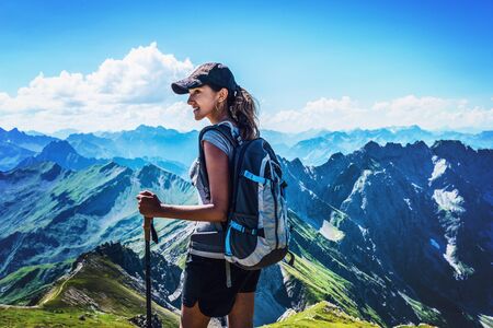 Attractive young woman trekking in the Allgau Alps on Grosser Daumen turning to watch something to the side with a smile against a backdrop of high rugged alpine mountainsの写真素材