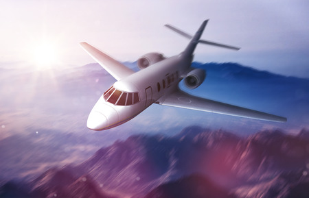 Luxury private jet flying over mountains shrouded in thin tendrils of mist at sunrise with the sun rising over the horizonの写真素材