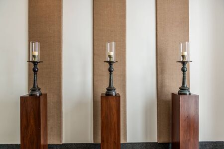 Three candles and candelabra on wooden plinths in a luxury interior with textile panels on the wallのeditorial素材