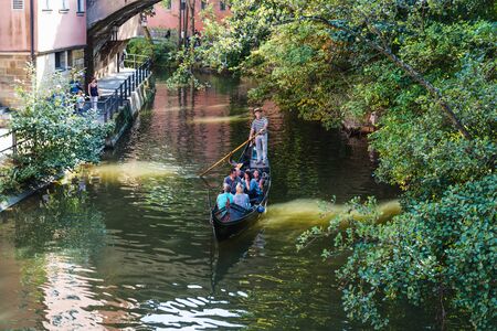 Tourists on a gondola ride on the Regnitz River, Little Venice, Bamberg, Bavaria, germany viewed through leafy green branches of an overhanging treeのeditorial素材