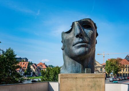 Modern sculpture of a bronze face mask by Igor Mitoraj in Little Venice, Bamberg, Germany against a sunny blue summer skyのeditorial素材