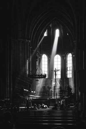 Beams of light shining into the historic interior of Bamberg Cathedral illuminating the alter and crucifix with the heads of members of the congregation praying in the pewsのeditorial素材