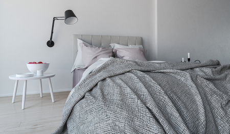 Messy unmade grey bed viewed from the foot in a monochromatic gray bedroom interior with wall-mounted angle poise lamp, 3d renderの写真素材