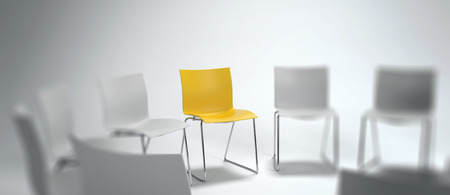 Panoramic banner of a single yellow chair in a group of blurred white ones arranged in a circle in a concept of leadership, achievement and diversity. 3d rendering.の写真素材