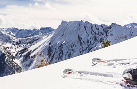 Person wearing skis standing in fresh pristine white winter snow overlooking a steep valley and snow-covered alpine peaks below, close up on the front of the skisの写真素材