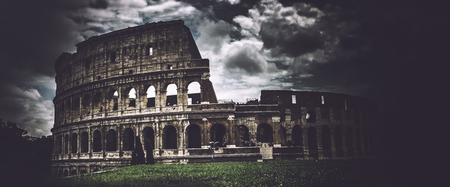 Panoramic view of Coliseum over green loan against dramatic clouds on darkened with vignette effect...