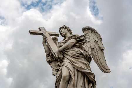 The famous statue Angel With The Cross, on the Ponte Saint Angelo across the river Tiber, Rome, Italy against a cloudy sky viewed low angleの写真素材
