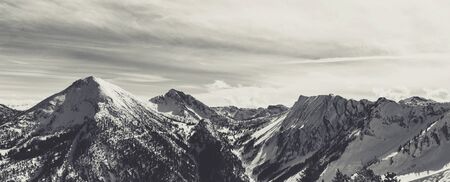 Monochrome view of mountain peaks covered with snow and grey cloudy sky on background