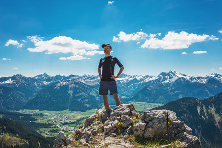 Successful and confident hiker on mountain summit with his hands on his hipsの写真素材