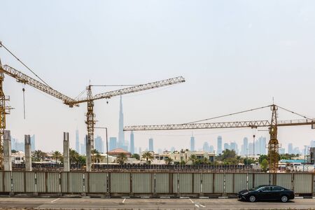 Construction Cranes in Front of Hazy City Skyline with Super Skyscraper Burj Khalifa on Sunny Day, Dubai, United Arab Emiratesの写真素材