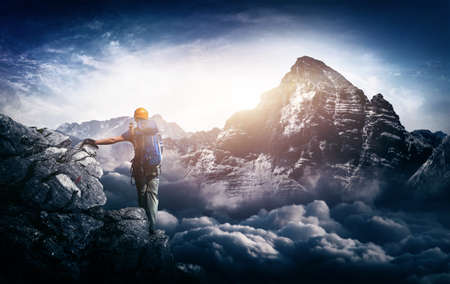 A mountain climber with a majestic sunrise view over towering snow capped mountains and cloud tops.の写真素材