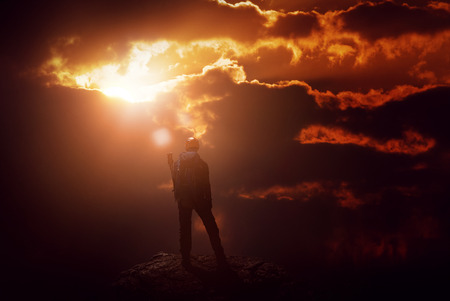 A mountain climber on a peak is silhouetted by an intense, fiery red sunset.の写真素材