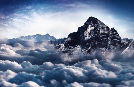 A majestic, snow capped rugged mountain peak towers above the cloud tops.の写真素材