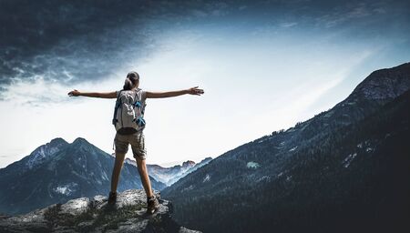 Rear view of female hiker spreading arms while standing on rock in mountainsの写真素材