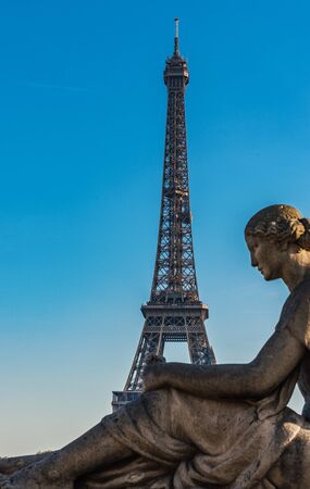 Eiffel Tower, Paris, France viewed against a sunny blue sky behind the statue of a seated woman in the foreground in a travel conceptの写真素材