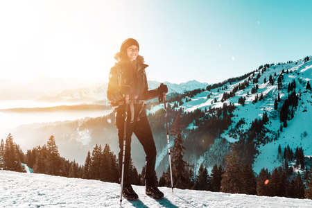 Portrait of smiling female hiker standing with poles in winter snowy mountainsの写真素材