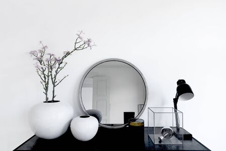 Close up on mirror and plant pots next to lamp and metal trinket in transparent box on modern black table. 3d renderingの写真素材