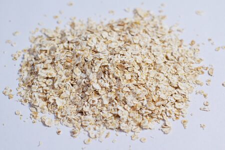 Pile oatmeal flakes scattered on a white background.