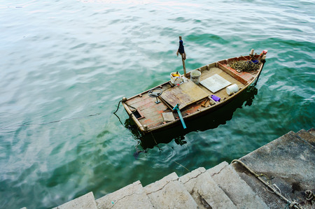 There is a small boat parking at a concrete dock, the boat looks old and messy with old paint cans and steering wheelの写真素材