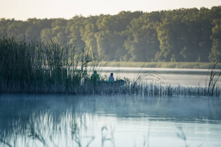 Fishermen in the reeds on the lake in a boat fishing at sunriseの写真素材