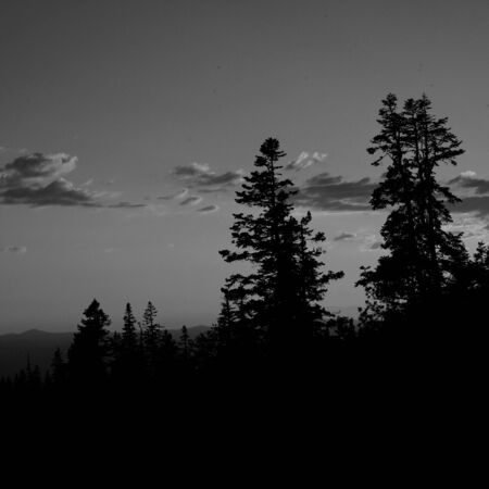 The sun sets in Central Oregon with brilliant reds and oranges in the sky and clouds with tall pine trees in the foreground,.の写真素材