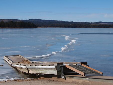 A short boat dock extends into the frozen over waters with a rugged ice path of Thompson Reservoir in Southern Oregon on a sunny winter day.の写真素材
