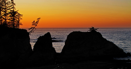 Sunset over the Pacific Ocean on Oregon's Central Coast with cliffs and trees in the foreground and ocean and colorful sky in the background in the summer.の写真素材
