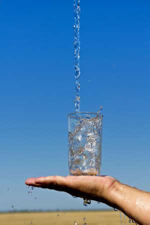 Water pours into the glass, which is on the palm of your handの写真素材