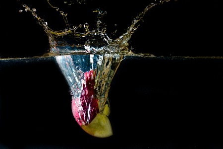 bitten apple dropped into water and created a water splashの写真素材