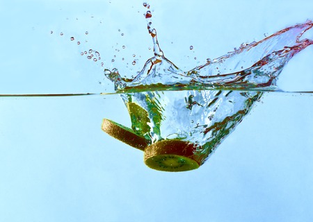 chopped kiwi dropped into water and created a water splashの写真素材
