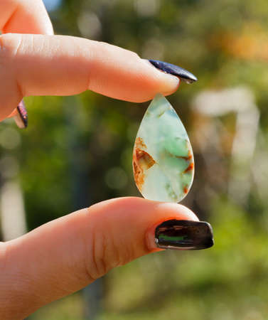 semi-precious stone chrysoprase in woman's hands on a blurred colorful backgroundの写真素材