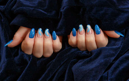 Female hands with a multicolored manicure on dark blue background closeupの写真素材