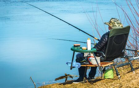 fisherman sits in a chair on the beach with fishing rods and fishesの写真素材