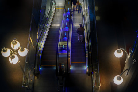 Top view of a brightly lit escalator with blue lights and decorative chandeliers, creating a modern urban atmosphereの写真素材