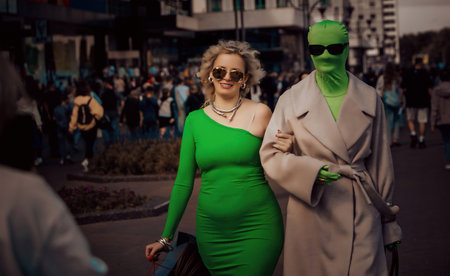 A woman in a green dress and a person in a bright costume walk among the crowd during a festive eventの写真素材