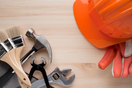 Hardhat, gloves and some assorted tools arranged on a wooden surface. Construction, repair or home...