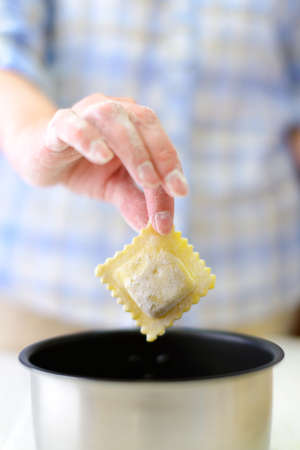 Cooking: woman hand holding single fresh raviolo over the saucepanの写真素材