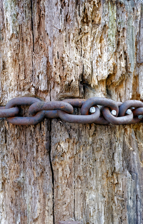 Backgrounds and textures: rusty metal chain over aged wooden pillarの写真素材