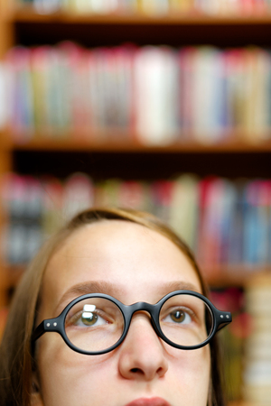 People: young girl, student, wearing eyeglasses, chooses a book in a library or bookstore, close-up portrait, intentional partial crop.の写真素材