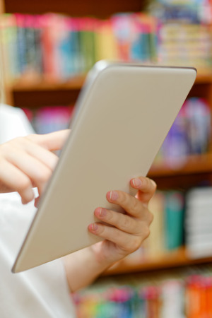 People: young girl, student, making use of tablet computer or e-book reader, in a library or bookstoreの写真素材