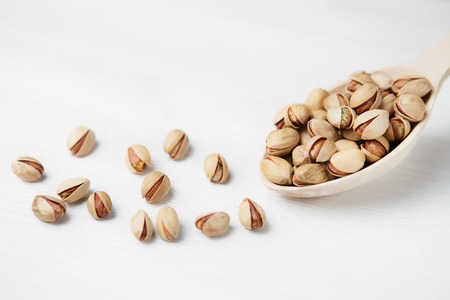 Pistachios on wooden spoon over white wood background.