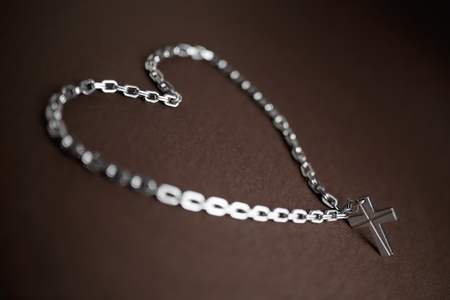 Silver christian cross and chain on brown background with heart symbol.の写真素材